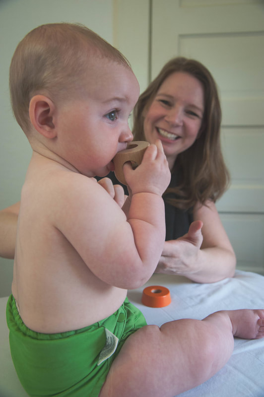 Image shows baby playing with toy while acupuncturist looks on.